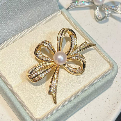 Gold bow-shaped brooch with a pearl center on a light blue jewelry box.